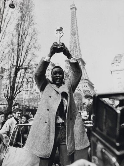 Photo noir et blanc de Pelé dans les rues de Paris brandissant la Coupe du monde dite trophée Jules Rimet